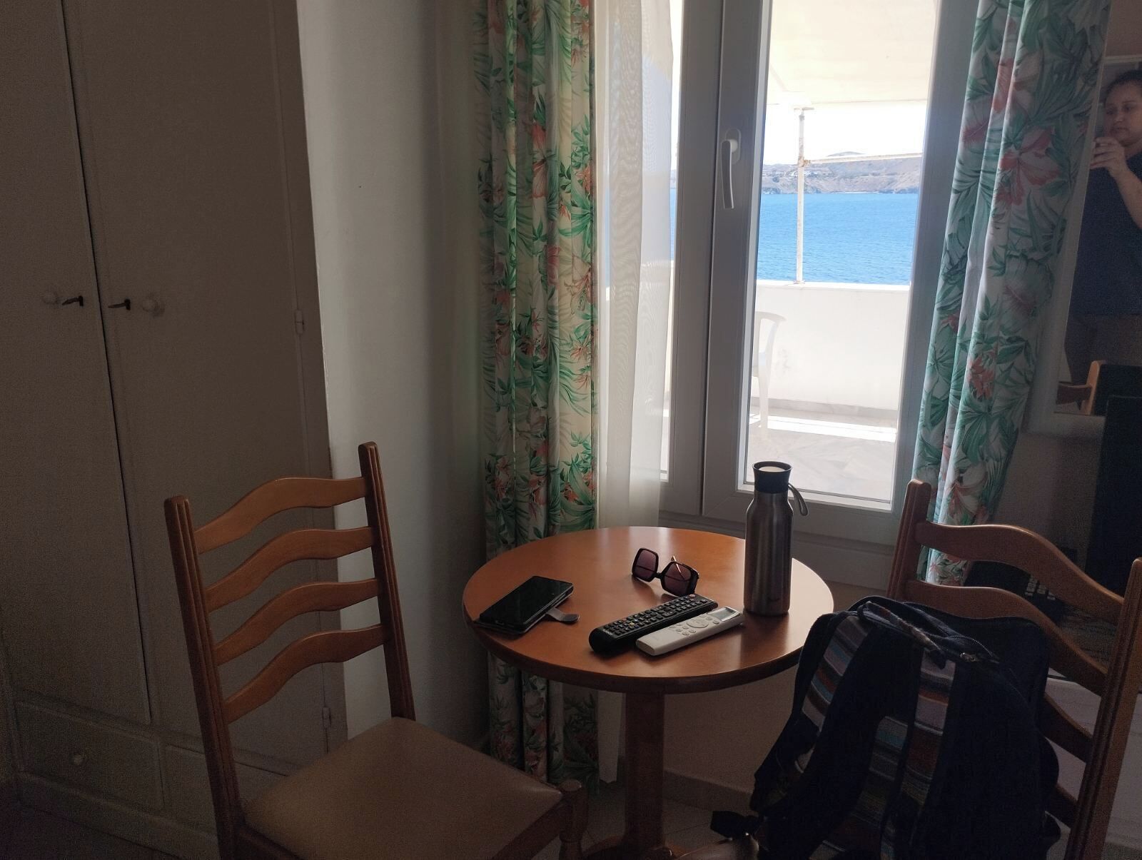Ein Zimmer mit einem Holzhocker, einem kleinen runden Tisch, einem Smartphone, einer Fernbedienung und einer Wasserflasche.
