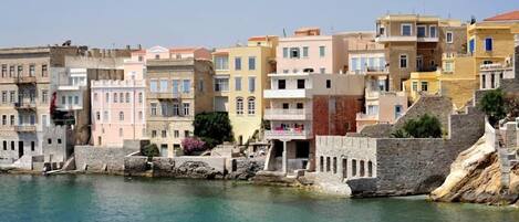 A coastal town with buildings along the waterfront, featuring stone walls and balconies.