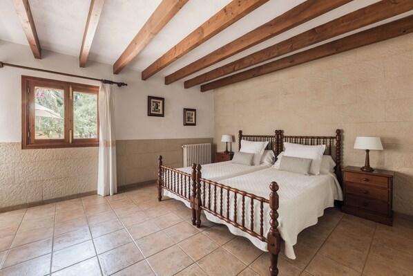 Un dormitorio con una cama de madera, dos mesitas de noche, un ventanal con cortinas y un radiador.