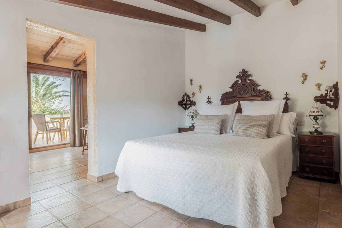 A bedroom with a bed, wooden headboard, bedside tables, and a view to an outdoor patio.