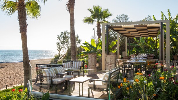 Patio exterior con asientos y una mesa lista para comer, con vistas a la playa.