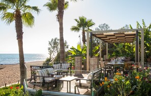 An outdoor patio with seating and a table set for dining, overlooking a beach. - Ionion Beach Apartment Hotel (Pineios)