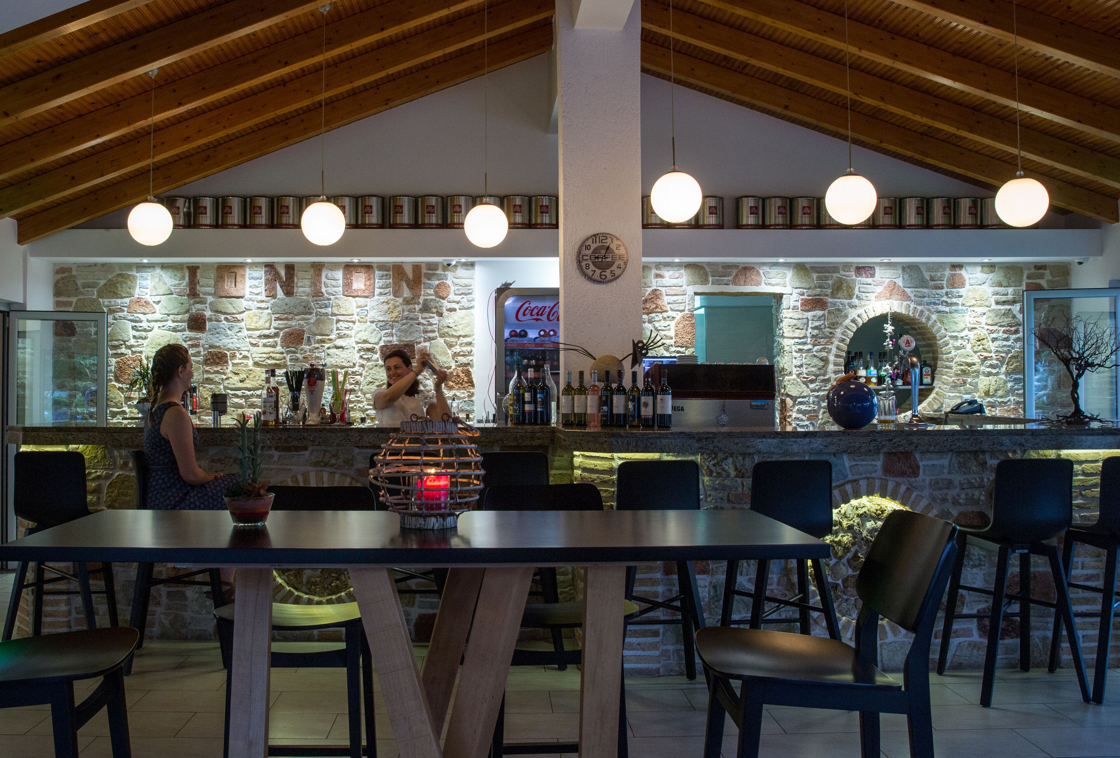 A restaurant with a stone wall, wooden ceiling, and a bar area with a Coca-Cola sign.
