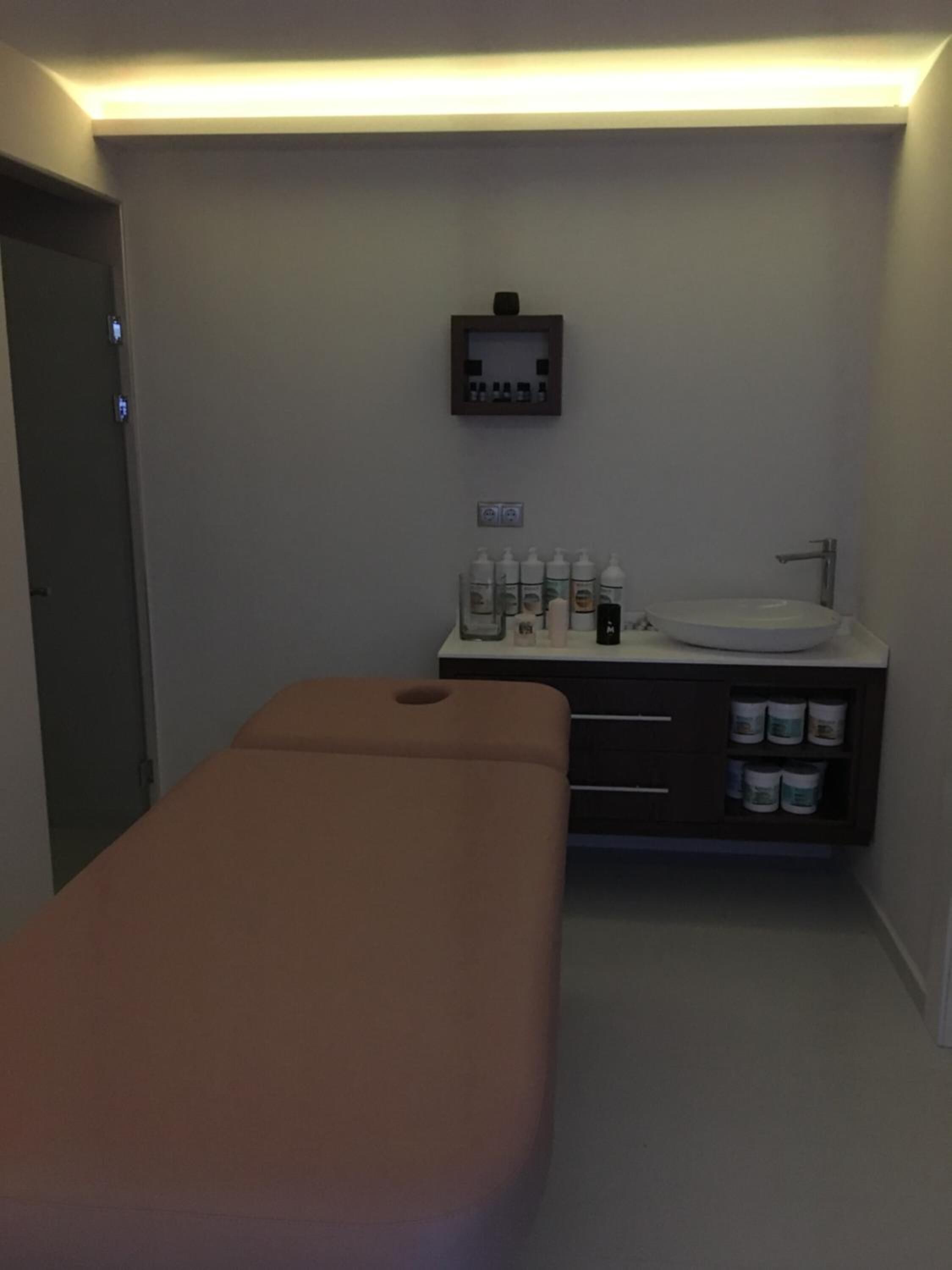 Une pièce équipée d’une table de massage, d’un petit lavabo avec des articles de toilette et d’un panneau de commande fixé au mur.