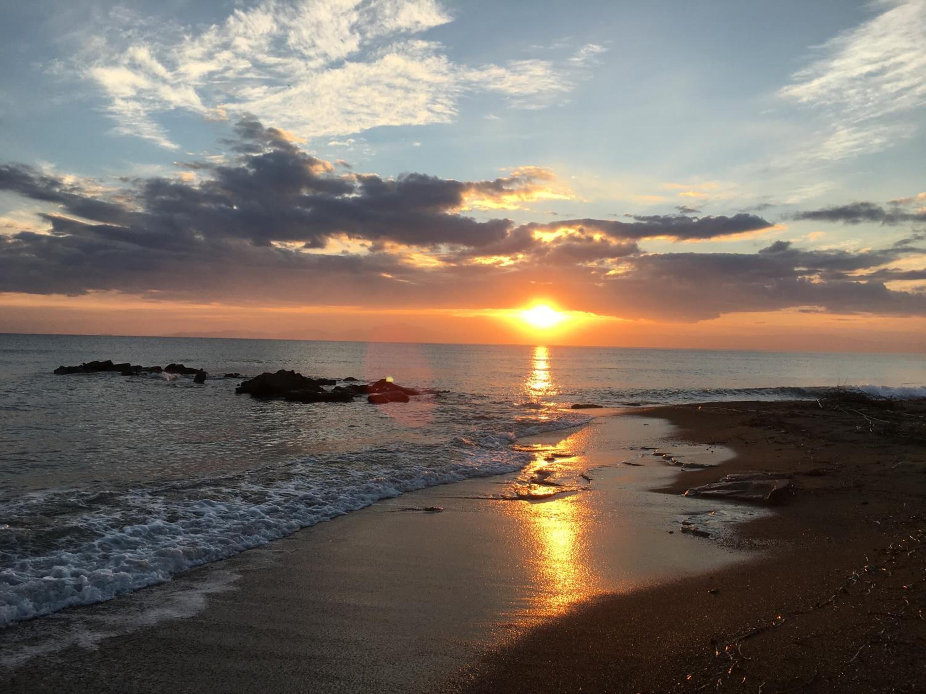 Un atardecer sobre una playa con olas, rocas y un cielo despejado.
