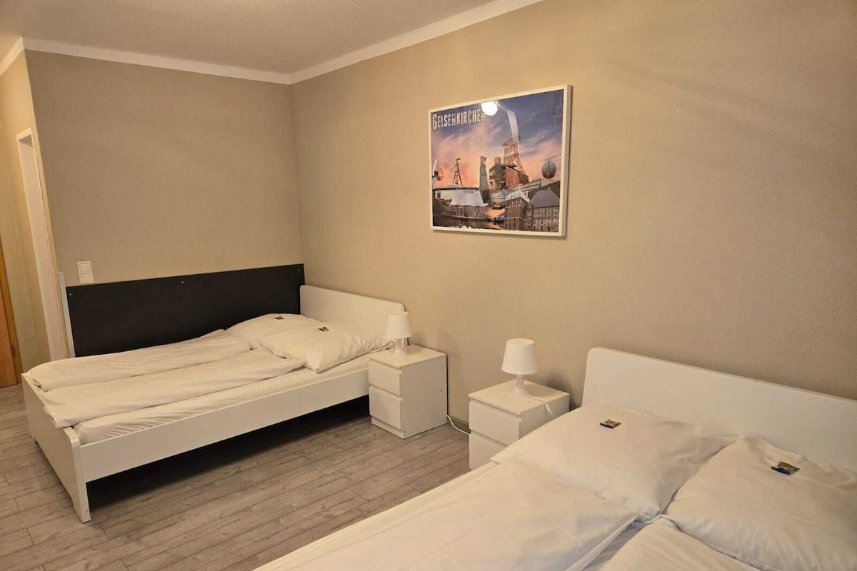 Ein Hotelzimmer mit zwei Einzelbetten, einem Nachttisch mit Lampe und einem Poster an der Wand.