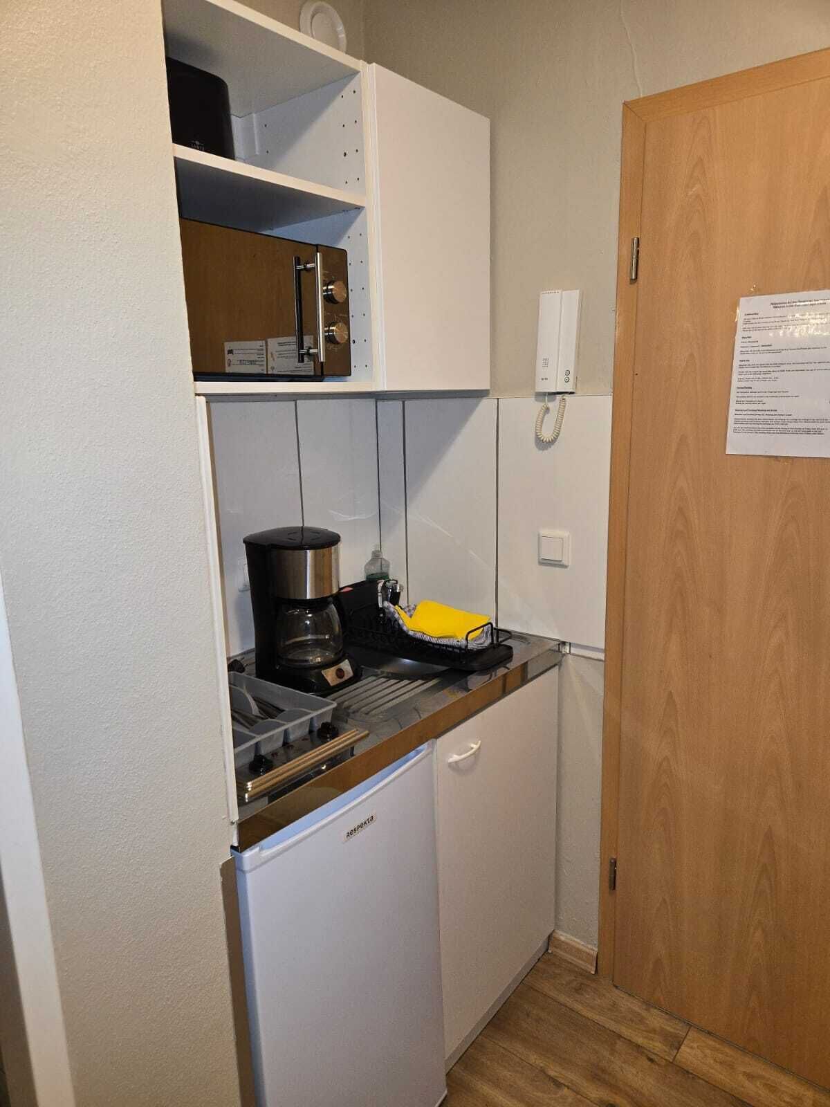 Una kitchenette compacta con cafetera, un escurreplatos amarillo y un refrigerador blanco.