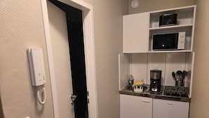 Een compacte kitchenette met een magnetron, koffiezetapparaat en bestek op het aanrecht.