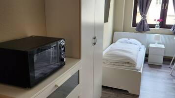 Una camera da letto con un letto, un armadio bianco, un comodino, una lampada e una finestra con tende.