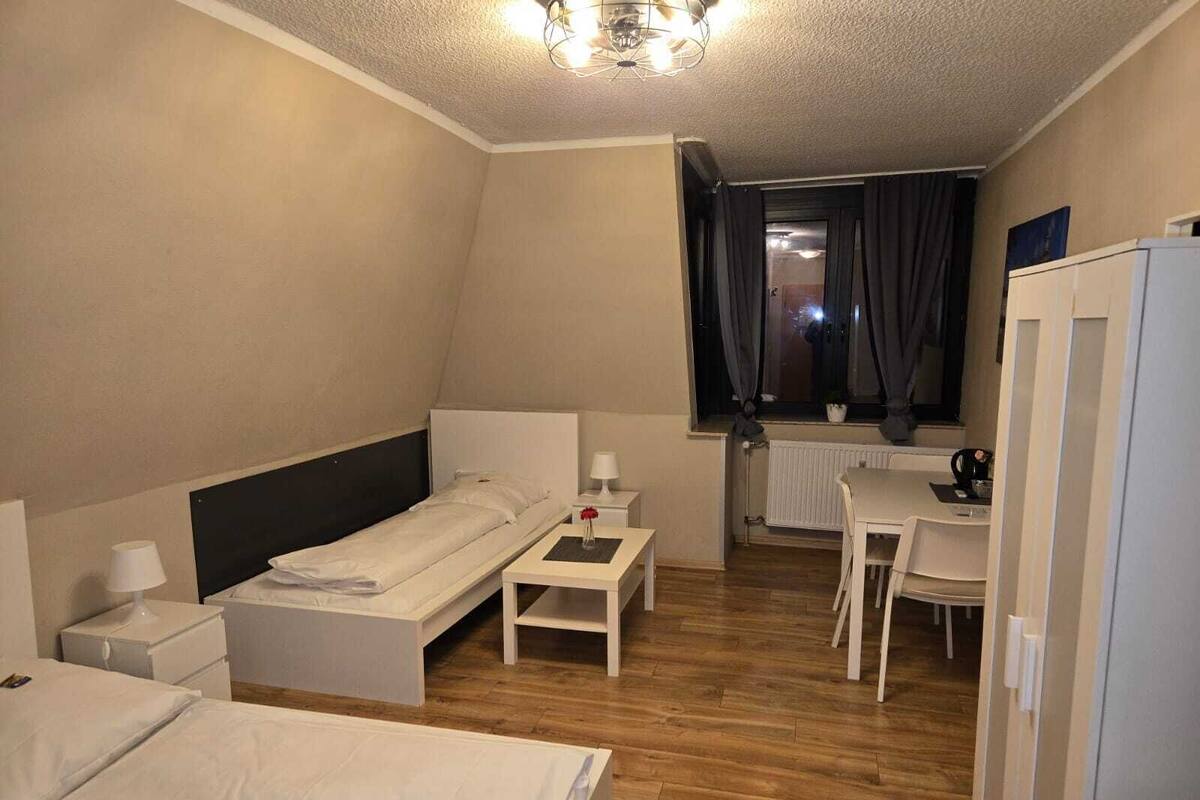 Ein Hotelzimmer mit zwei Betten, einem Schreibtisch, einem Stuhl, einem Heizkörper und einem fenster mit Vorhängen.
