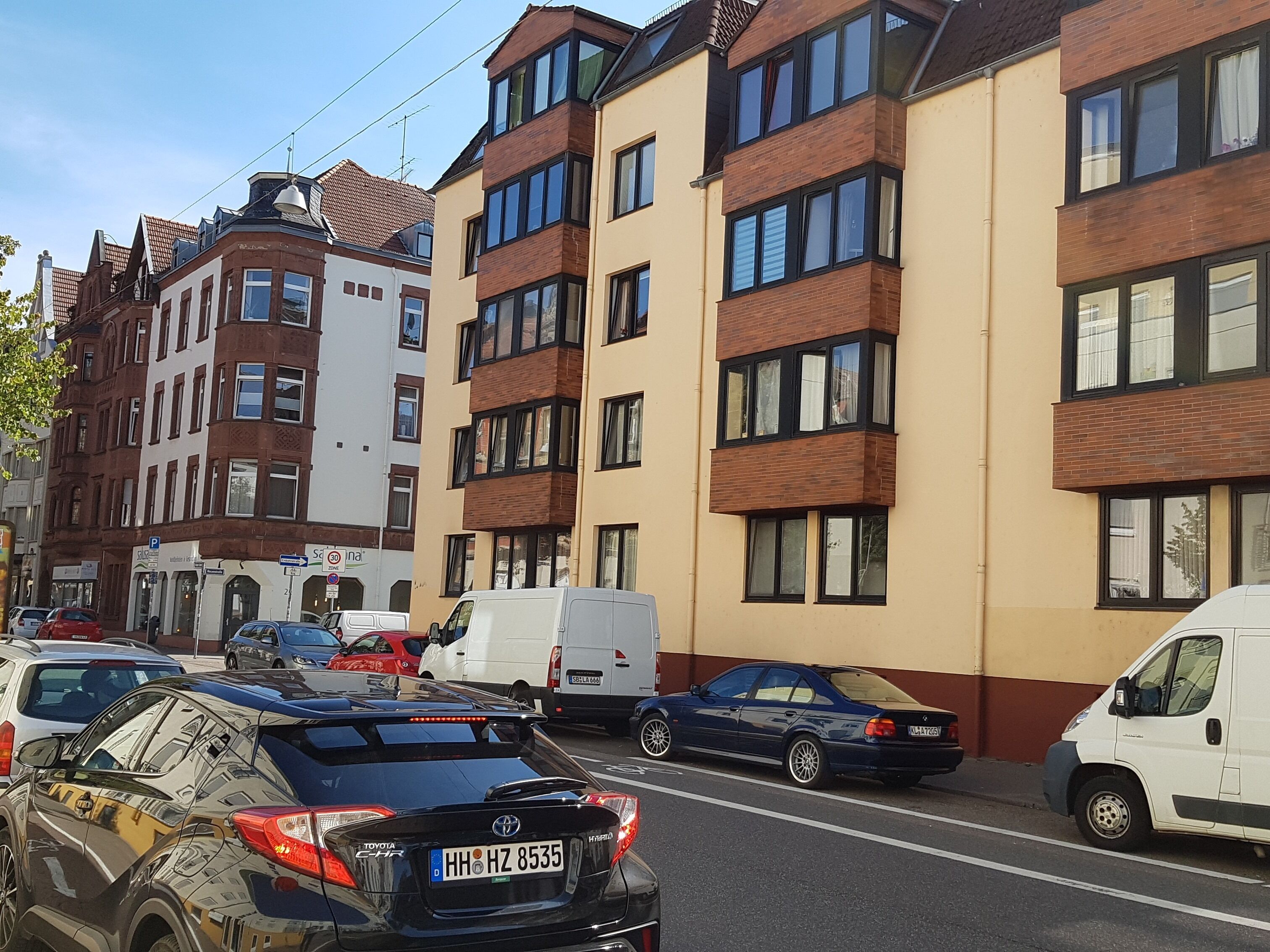 Une rue bordée de voitures garées et d’immeubles à plusieurs étages.