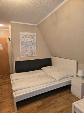 A bedroom with a single bed, a nightstand, a lamp, and a poster on the wall.