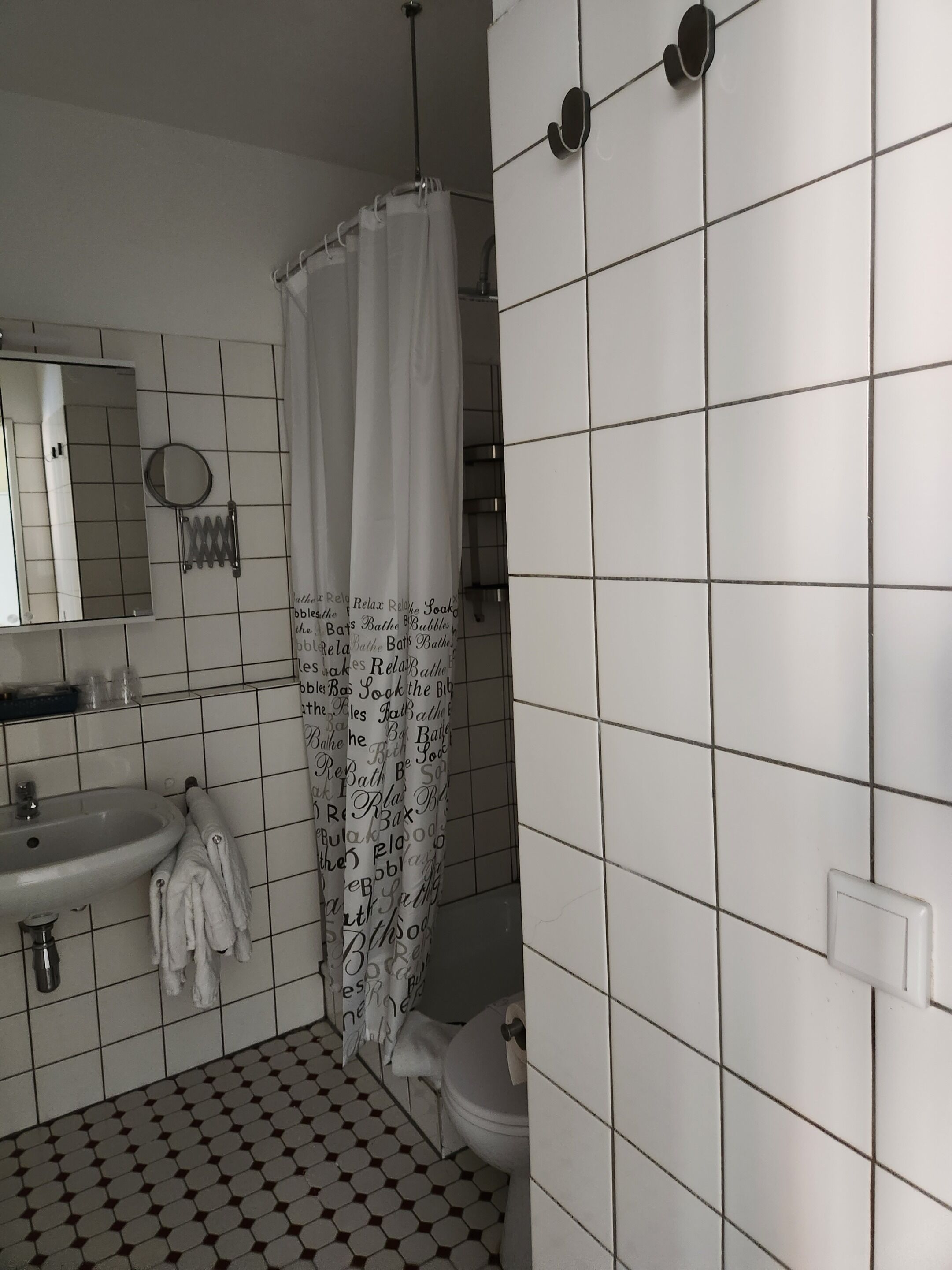 A bathroom with a white sink, a mirror, a toilet, and a shower curtain with text.