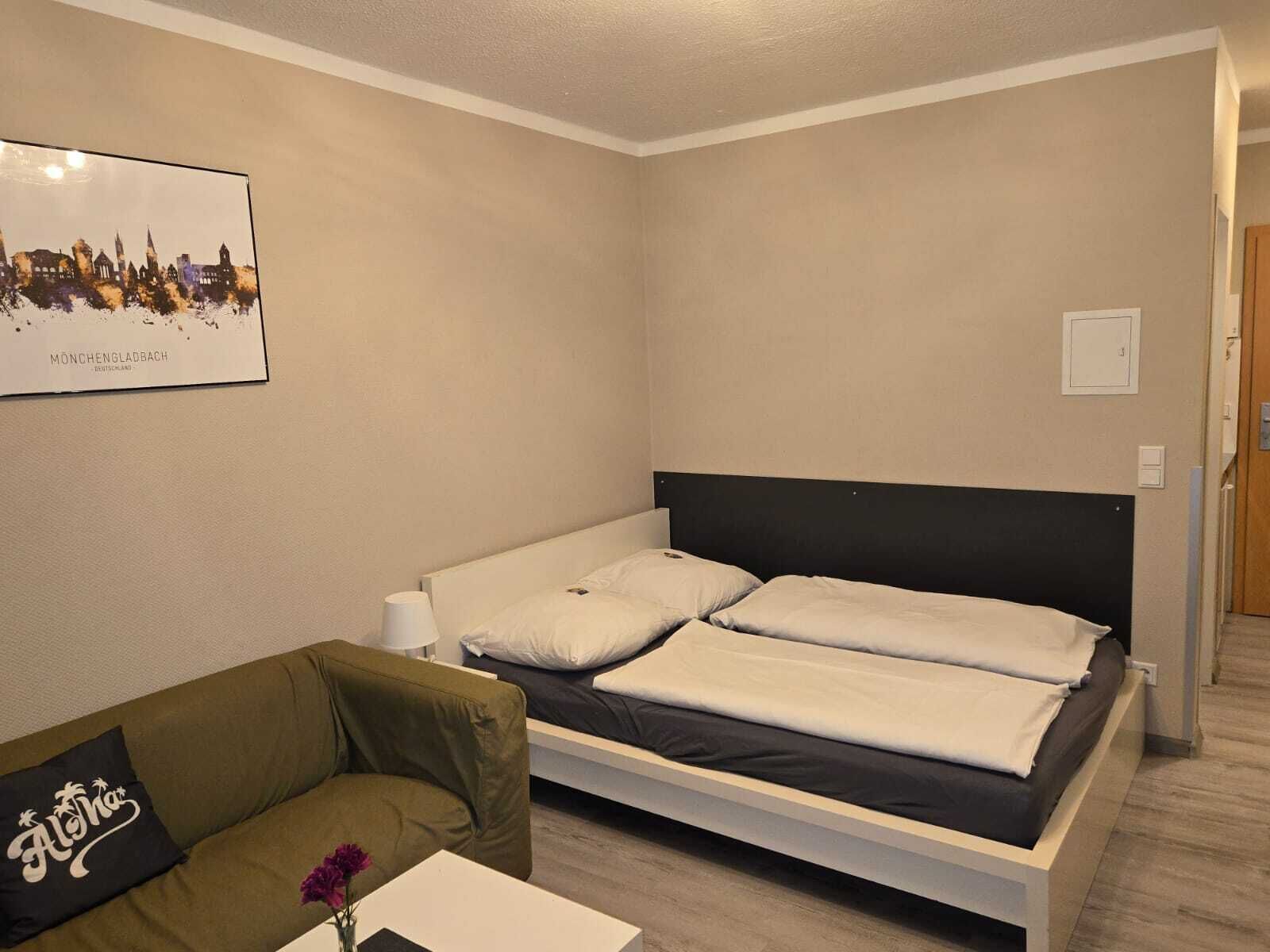 Una camera d'albergo con un letto, un divano, un tavolino con un vaso e un quadro appeso al muro.