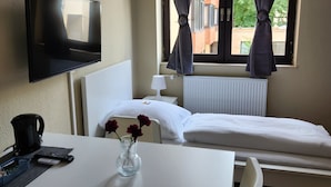 Een hotelkamer met een bed, een bureau, een televisie, een raam met gordijnen en een radiator.