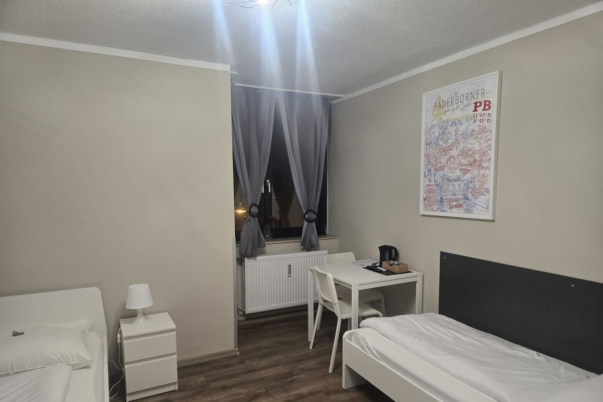 Ein Hotelzimmer mit Bett, Schreibtisch, Stuhl, Heizkörper und einem fensterbepflanzten Fenster.
