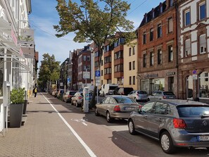 A street with parked cars and buildings, including a shop with a sign that reads "Pietro von Rüden".