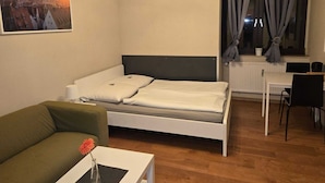 Een moderne, goed verlichte kamer met een bed, een klein tafeltje met een vaas, een groene bank en een zithoek met stoelen.