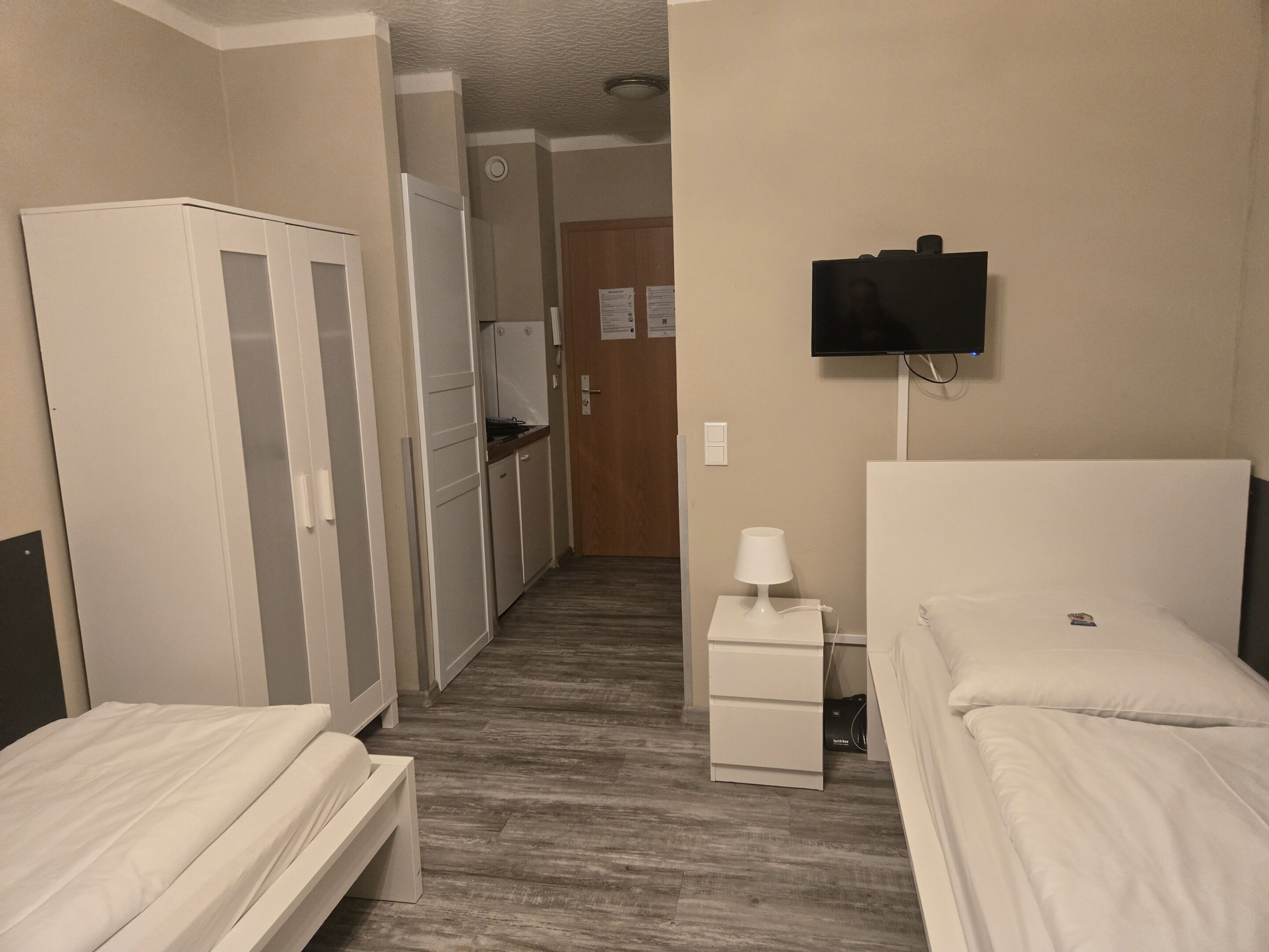 Een hotelkamer met twee bedden, een televisie, een klein tafeltje met een lamp en een kitchenette.