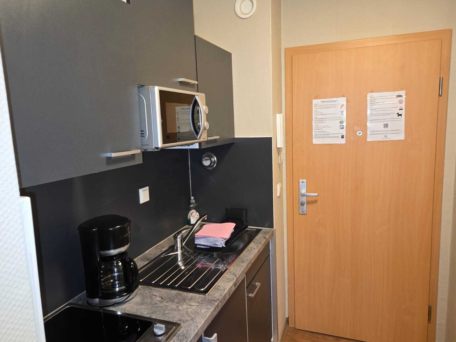 Una kitchenette compacta con microondas, cafetera y un lavamanos pequeño.