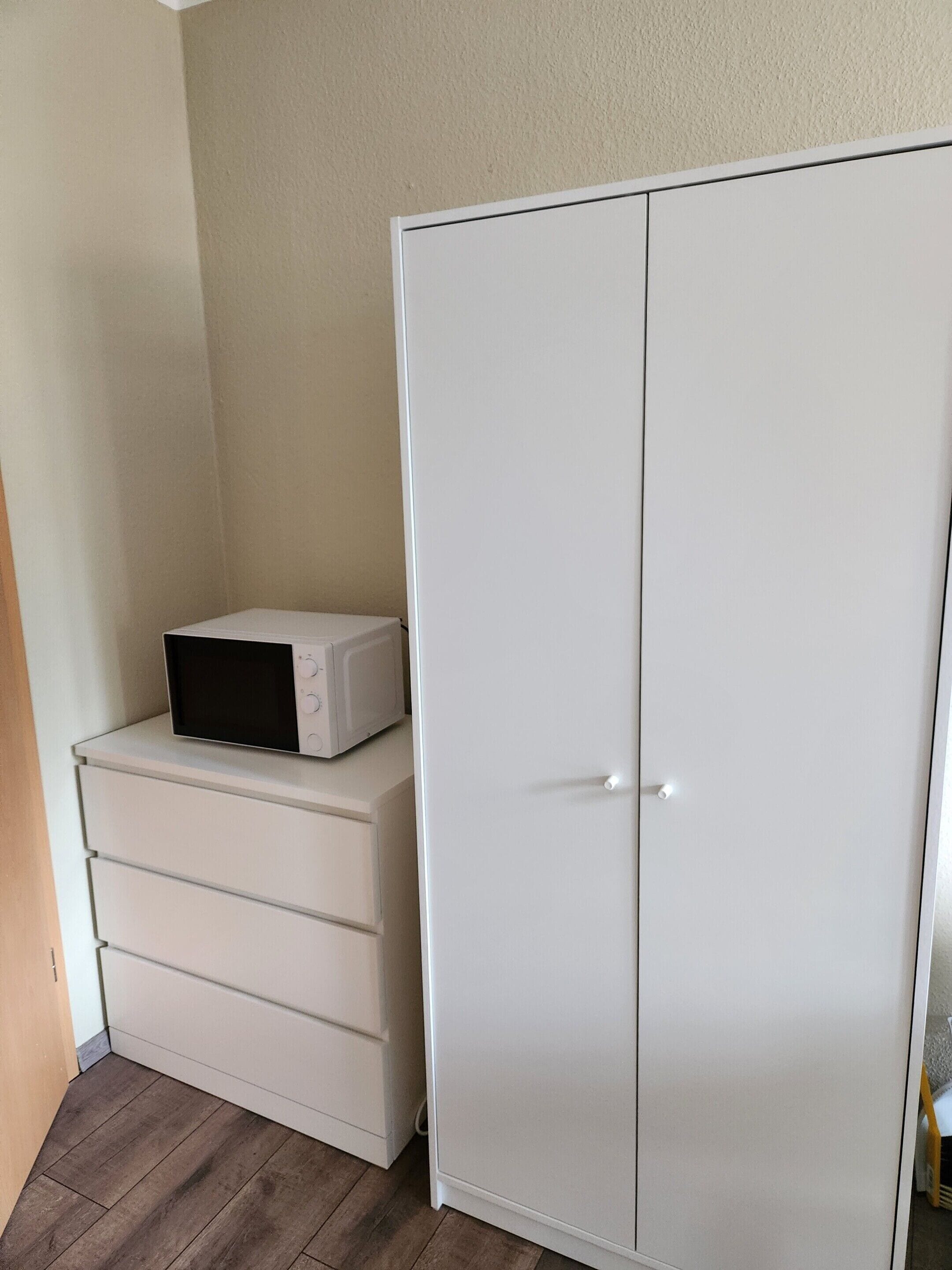 En vit garderob med en mikrovågsugn placerad ovanpå en vit byrå.