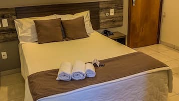 A neatly made bed with white and brown linens, a brown throw blanket, and rolled towels on a wooden headboard.