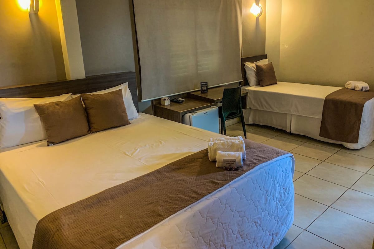 A hotel room with two single beds, a desk, a chair, and a TV.