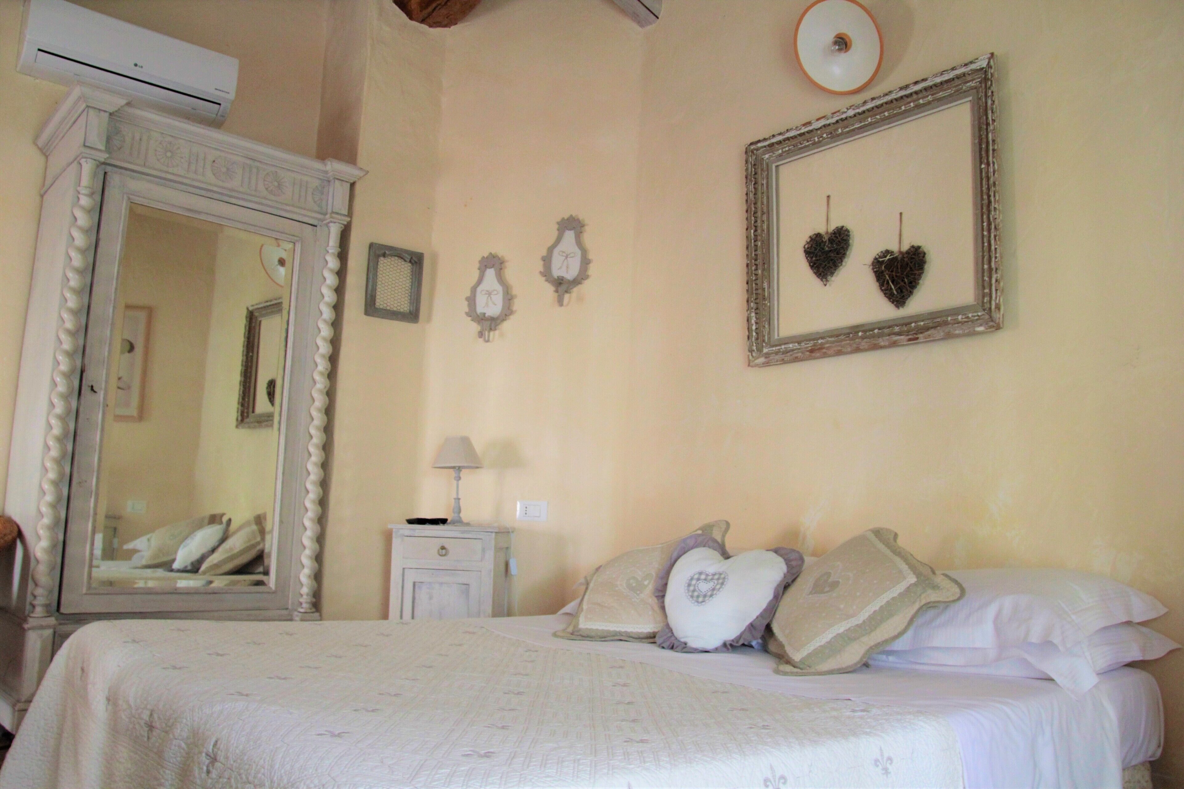 Une chambre avec un grand miroir, une table de chevet avec une lampe et un lit avec plusieurs oreillers.