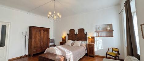 A spacious bedroom with a large bed, wooden wardrobe, and a chest of drawers.