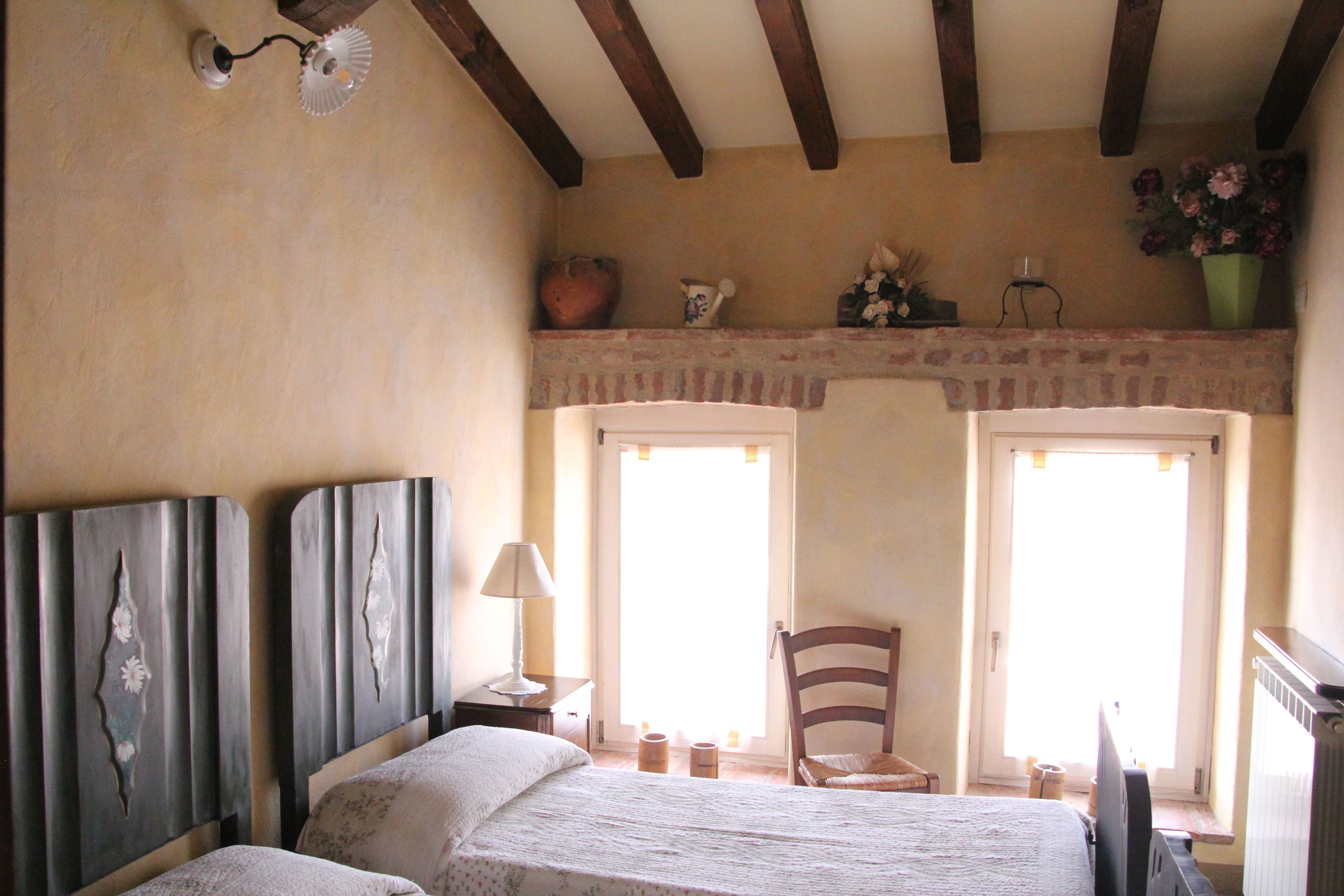 Una camera da letto con un letto, una sedia, un comodino, una lampada e una finestra con tende.