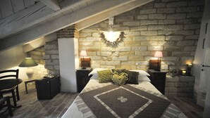 A bedroom with a stone wall, a bed with a quilt, two bedside lamps, and a chair. - Agriturismo Ca San Sebastiano Wine Resort & Spa (Camino)