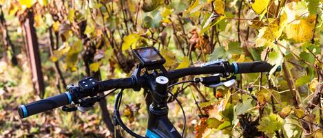 Una bicicleta eléctrica estacionada en un viñedo, con un dispositivo montado, posiblemente un GPS o teléfono.