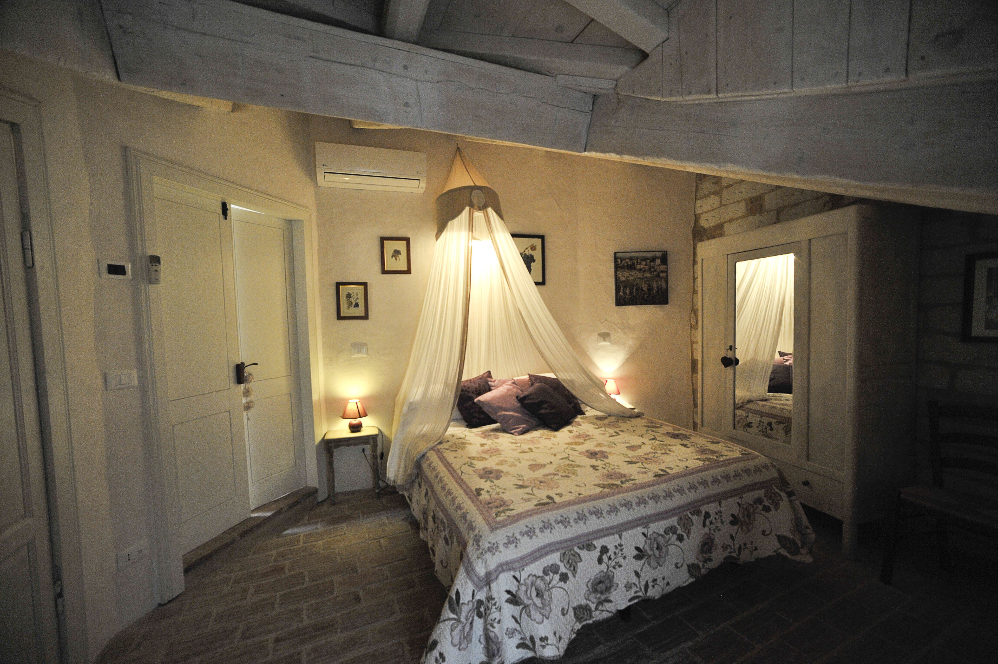 A bedroom with a bed under a canopy, a bedside table with a lamp, and a mirror on the wall.