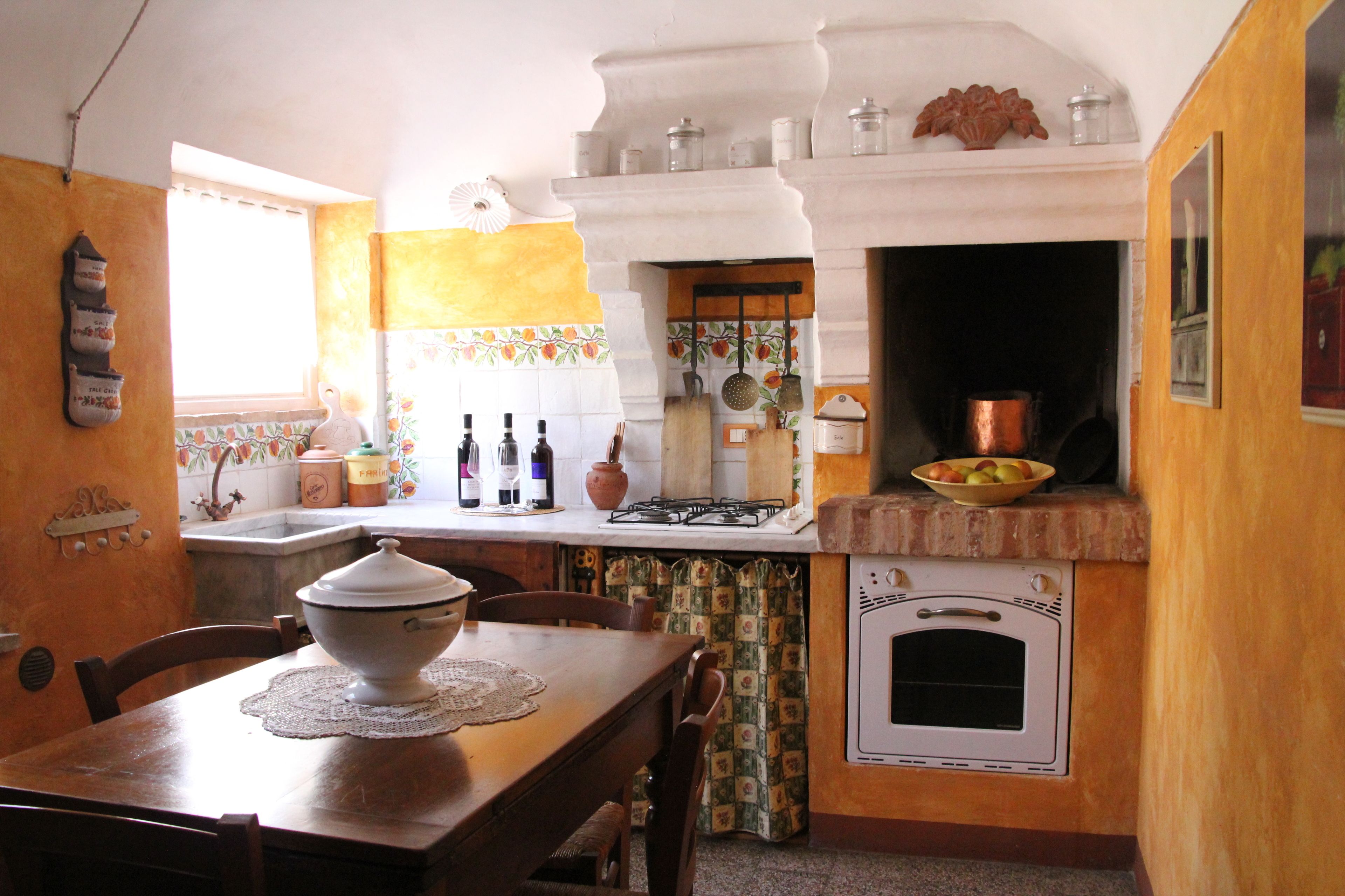 A kitchen with a wooden table, chairs, a stove, an oven, and a window with curtains.