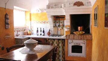 A kitchen with a wooden table, chairs, a stove, an oven, and a window with curtains.