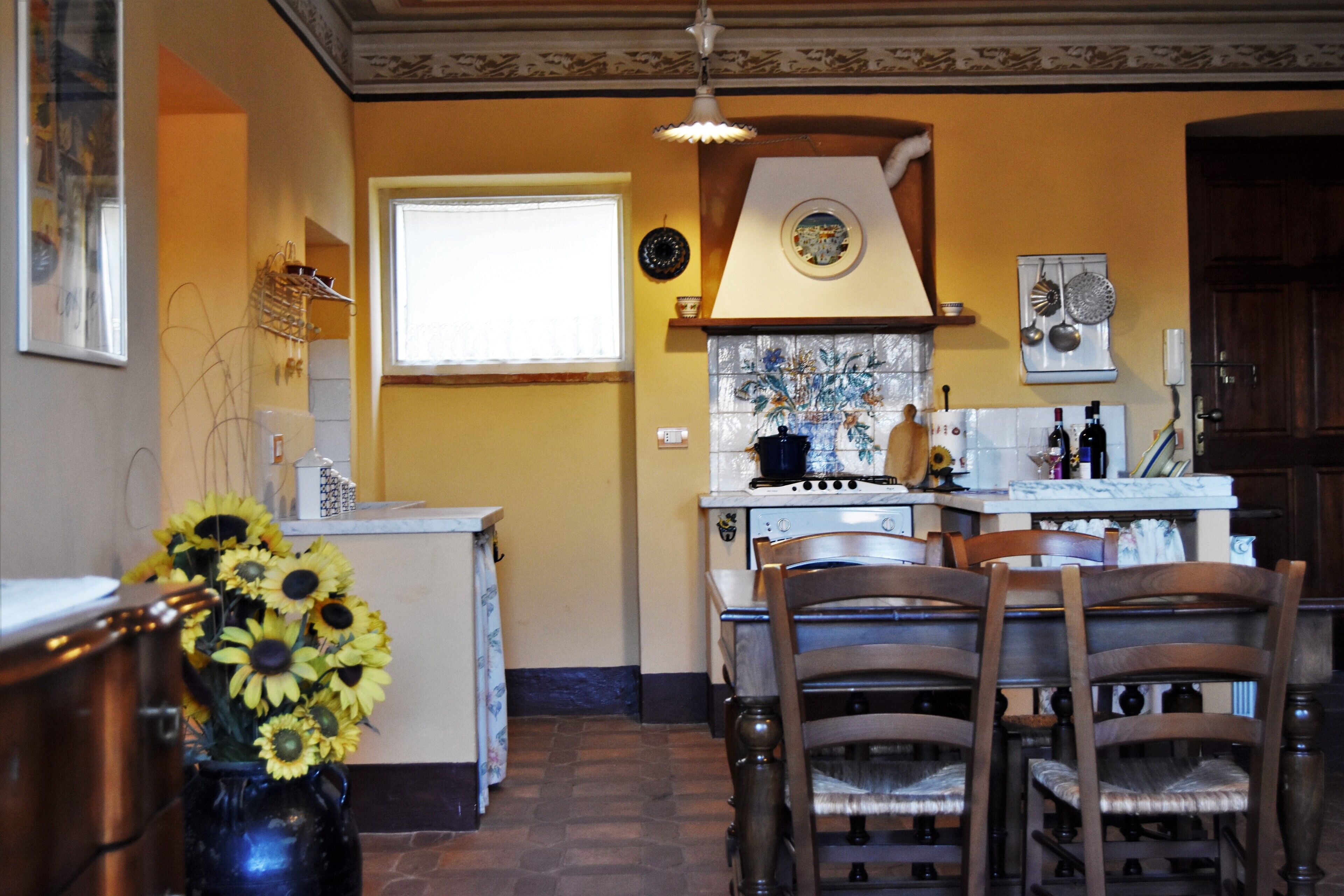 A kitchen with a dining area, featuring a stove, chairs, and a vase of sunflowers.