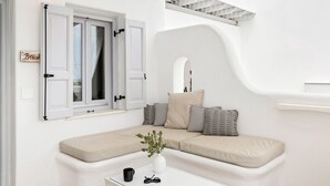 Una sala de estar moderna, con una decoración en tonos blancos, un sofá curvo, una mesita y una ventana con contraventanas.