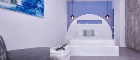 Un dormitorio moderno con una cama blanca curvada, un sofá gris y un cuadro abstracto azul en la pared.