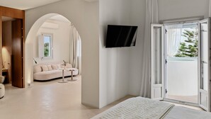 Una habitación de hotel moderna con una cama grande, un televisor montado en la pared y un balcón con vistas a árboles.