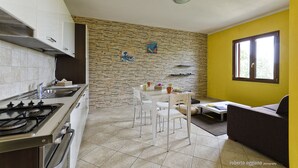 A modern kitchen with a gas stove, white cabinets, and a dining area with a table and chairs. - Residence L'isola Surf House (Palau)
