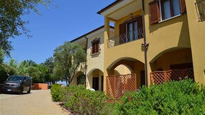 A two-story building with a yellow facade, arched balconies, and a car parked in front. - Residence L'isola Surf House (Palau)