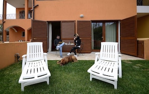 A patio with two white chairs, a dog, and two people seated at a table. - Residence L'isola Surf House (Palau)