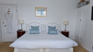 A neatly made bed with white bedding and two blue patterned pillows, flanked by two bedside tables with lamps, in a room with a white door and a framed picture on the wall. - Endeavour House (Cowes)
