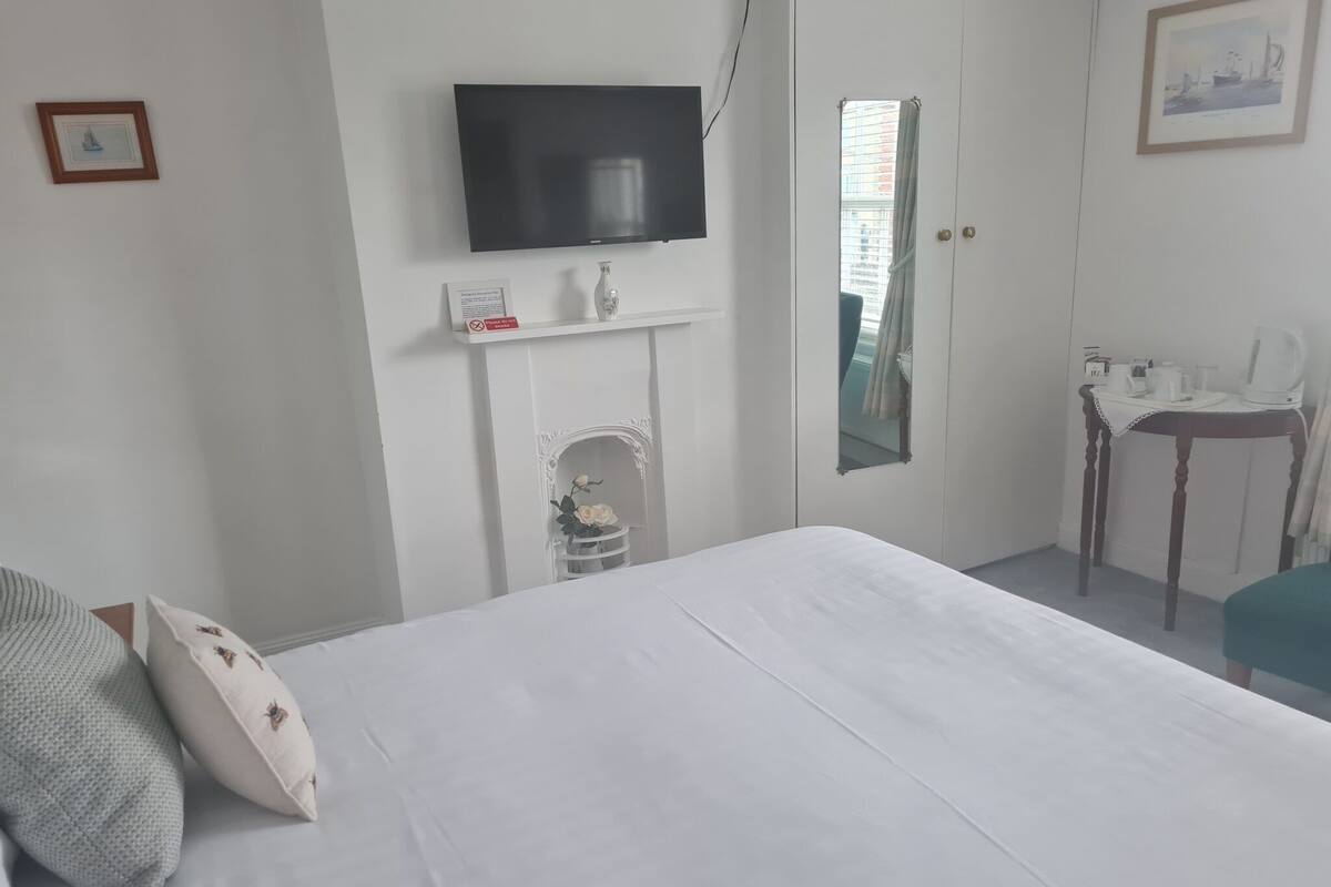 Une chambre d’hôtel comprenant un lit, un téléviseur à écran plat fixé au mur, une petite table avec une bouilloire et une chaise.