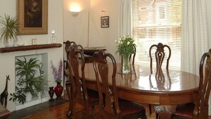 A dining room with a wooden table and chairs, a fireplace, and a large window with blinds. - Endeavour House (Cowes)