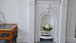 A white fireplace with a decorative arch and a vase of white flowers. - Endeavour House (Cowes)