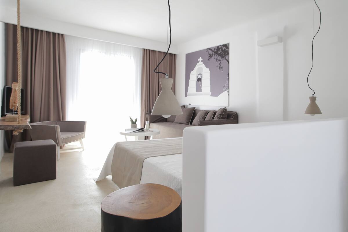 A modern hotel room with a bed, a sofa, a small table, and a TV.