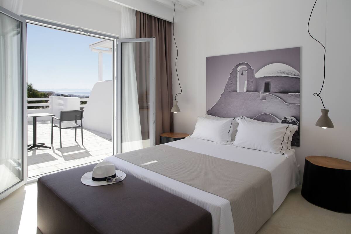 A modern hotel room with a large bed, a view of the outdoors, and a painting on the wall.
