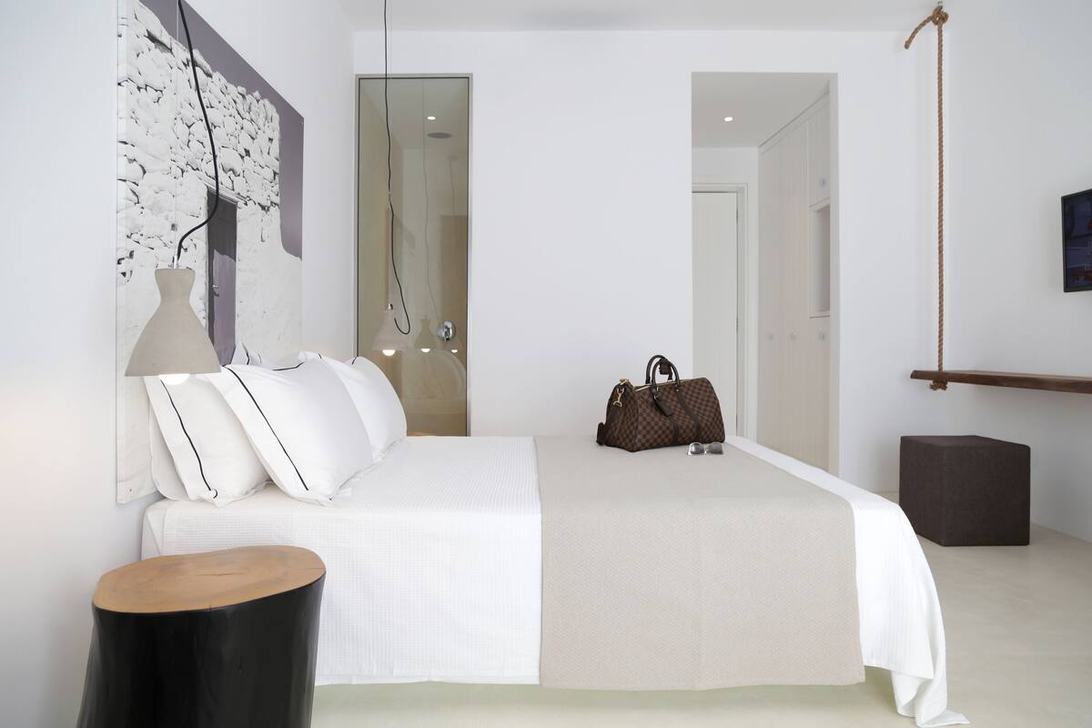 A modern bedroom with a large bed, a bedside table, a hanging light, and a wall-mounted TV.