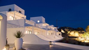 A modern building with a white facade, a large potted plant, and a well-lit outdoor area with rocks and plants. - Livin Mykonos Hotel - Adults Only by Mr and Mrs White (Mykonos)